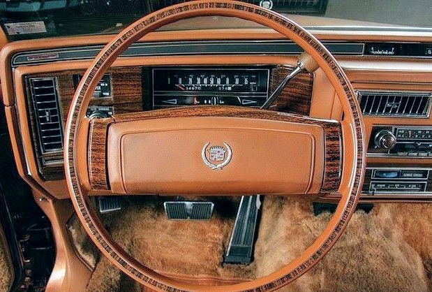 Classic Cadillac cockpit with a wood-grain steering wheel, matching burl dash trim and saddle leather