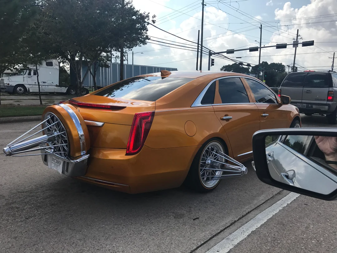 Orange candy Cadillac XTS slab on chrome wire swangas with a continental kit, rolling through a Houston intersection