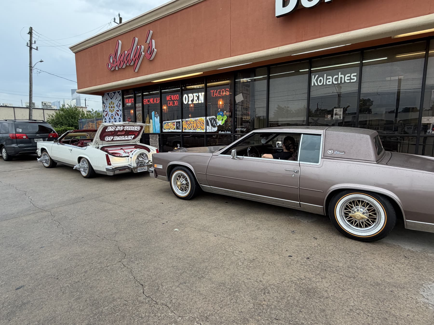 Two Cadillacs on wire wheels parked outside a Houston taqueria on a slab Sunday