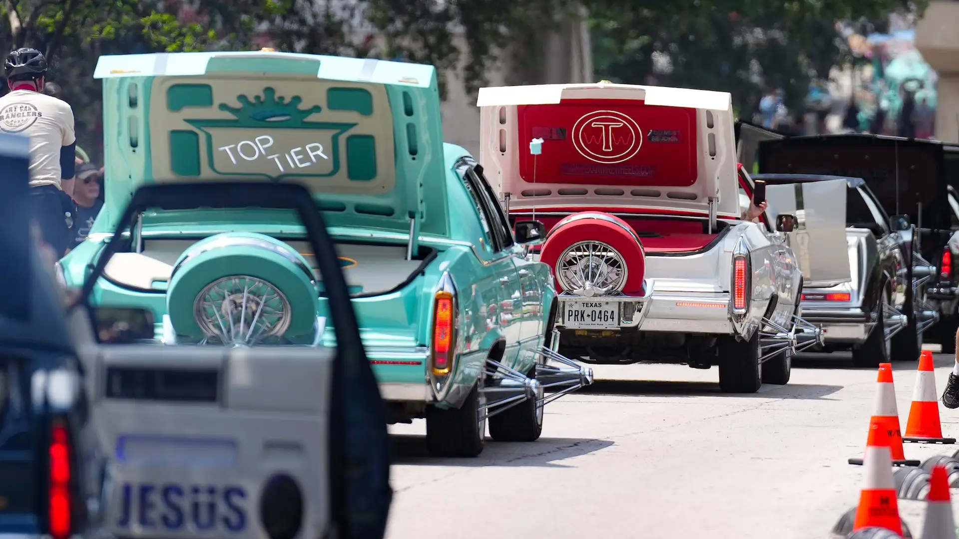 Row of Cadillac slabs with pop trunks open and wire wheels showing at a Houston street lineup